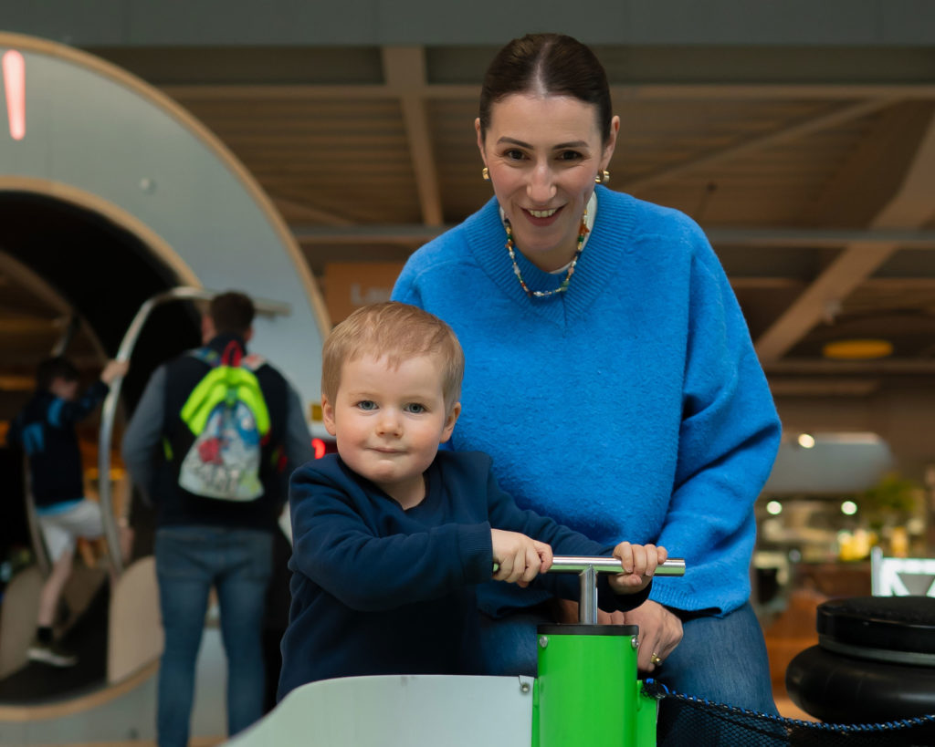 Woman in blue sweater and young child playing at an indoor amusement area, both smiling and enjoying their time together.