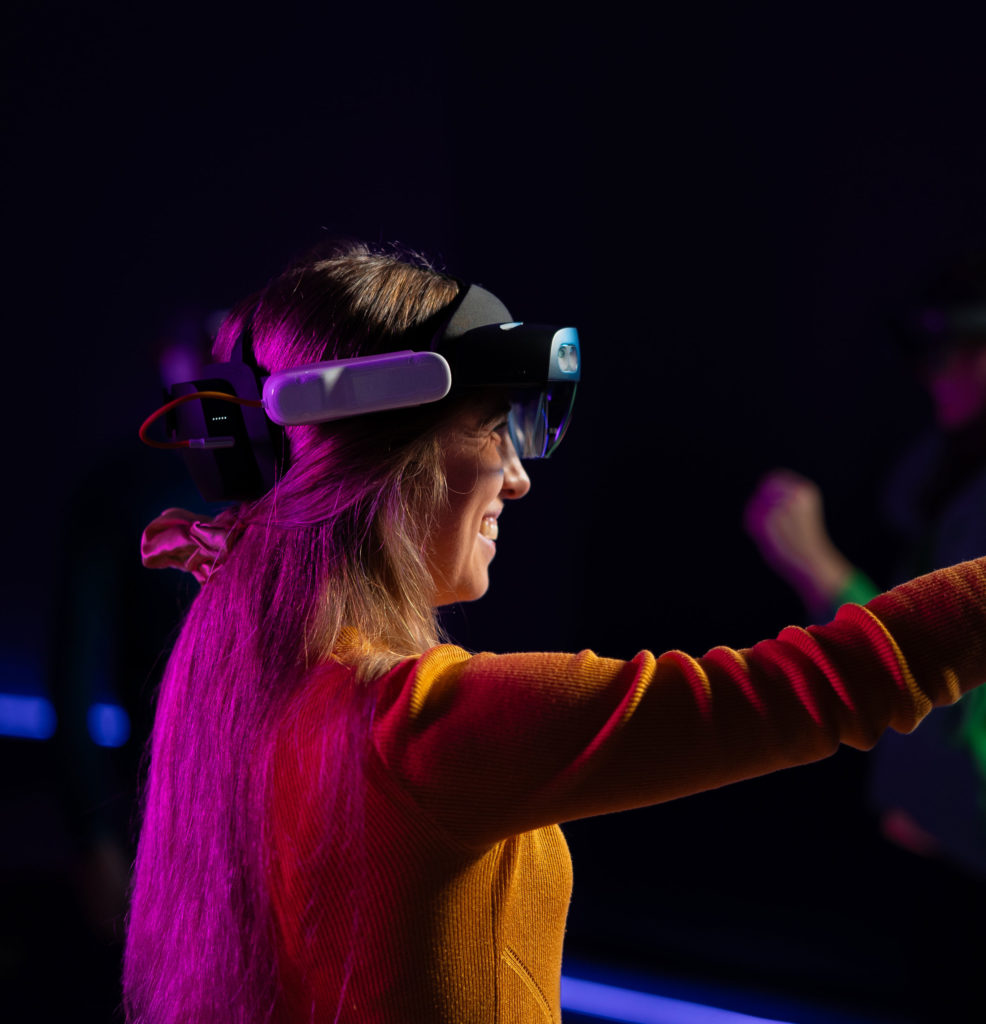 Woman enjoying virtual reality experience with headset in colorful lighting.