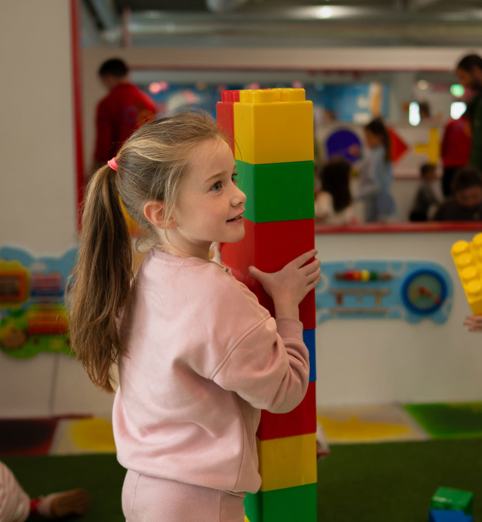 Child playing with large colorful building blocks indoors.