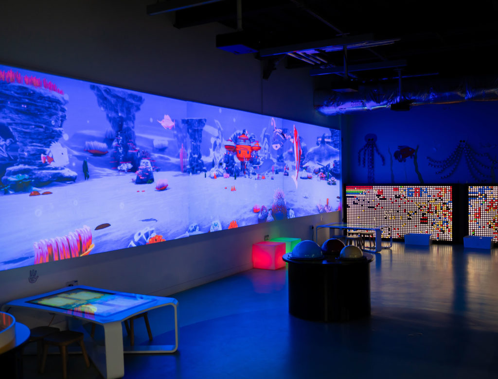 Interactive children's playroom with vibrant underwater-themed digital screens and colorful seating.