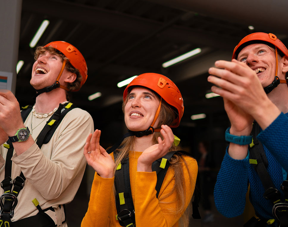 People wearing helmets and safety gear, smiling and clapping indoors.
