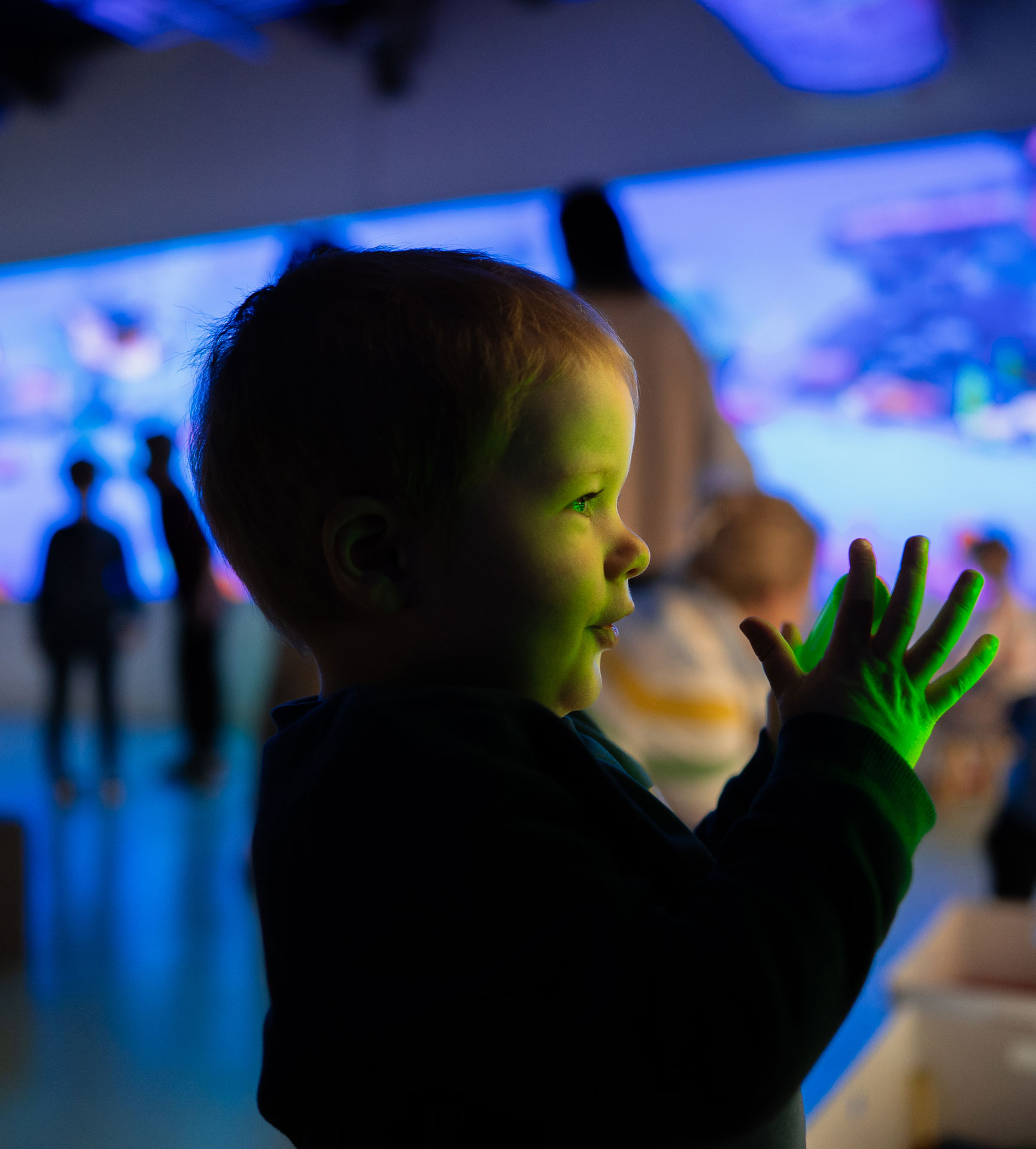 Toddler exploring a colorful, interactive digital exhibit with green light on hands.
