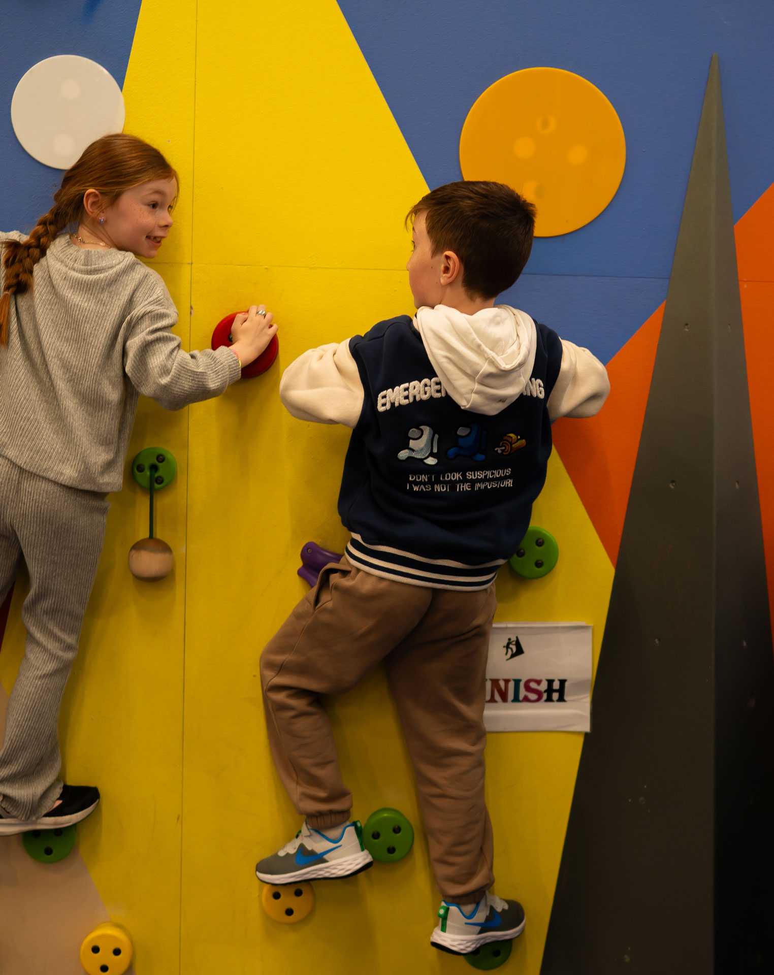Kids climbing a colorful indoor wall, smiling and enjoying the activity.