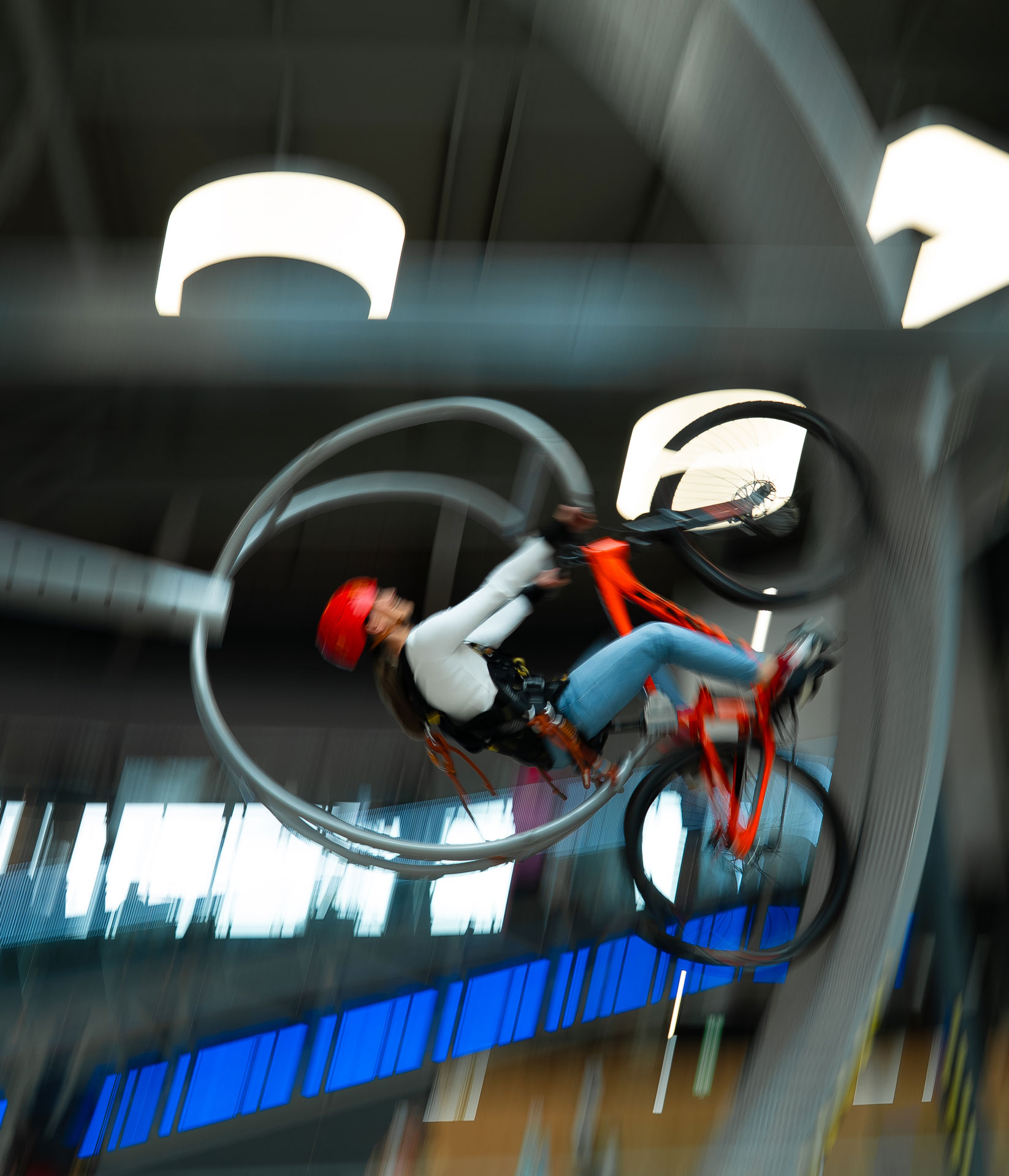 Person performing an indoor biking stunt on a loop track, wearing a helmet and safety gear.